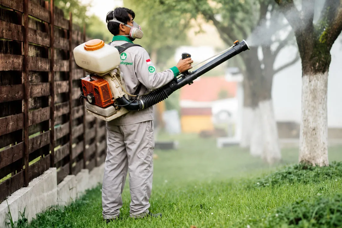 Petugas pest control Bali melakukan penyemprotan area taman menggunakan mesin mist blower untuk membasmi hama tanaman.